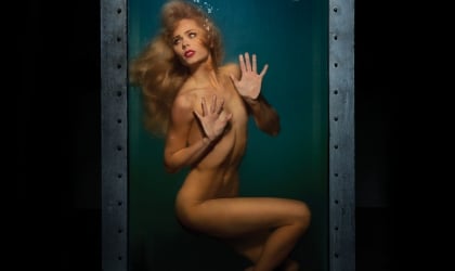 Laura Vandervoort poses nude in a cage with a Welcome to SeaWorld sign on it.