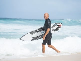 A man in a wetsuit walking with a surfboard.