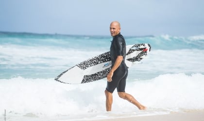 A man in a wetsuit walking with a surfboard.