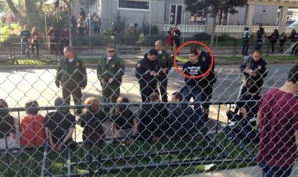 A group of people standing behind a chain link fence as PETA protester gets arrested