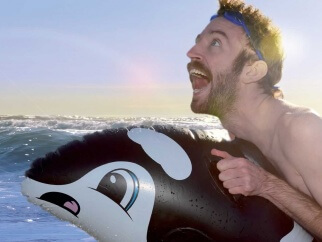 A man is riding an inflatable orca whale in the ocean.