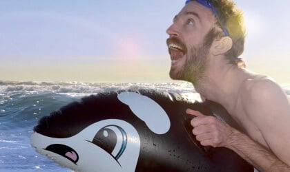A man is riding an inflatable orca whale in the ocean.
