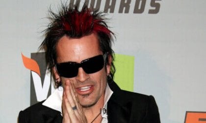 Tommy Lee, a man with red hair and tattoos, posing on a red carpet.