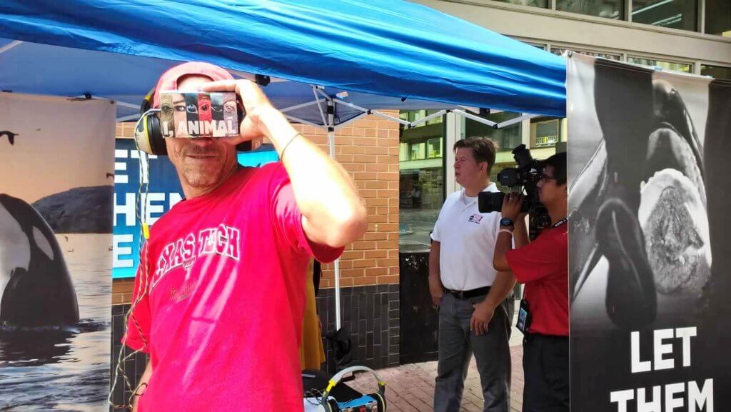 A man in a pink shirt is holding a virtual reality headset.