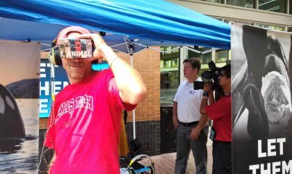 A man in a pink shirt is holding a virtual reality headset.
