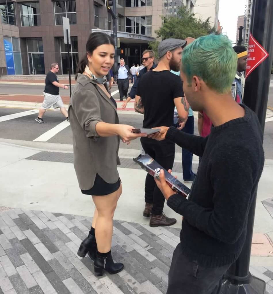 A man handing a woman a card on the street.