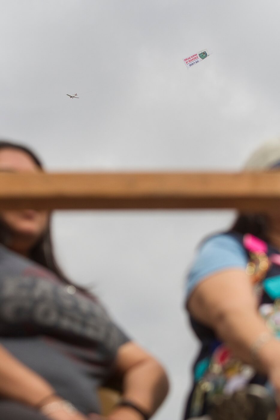 A group of people watching a kite banner fly in the sky.