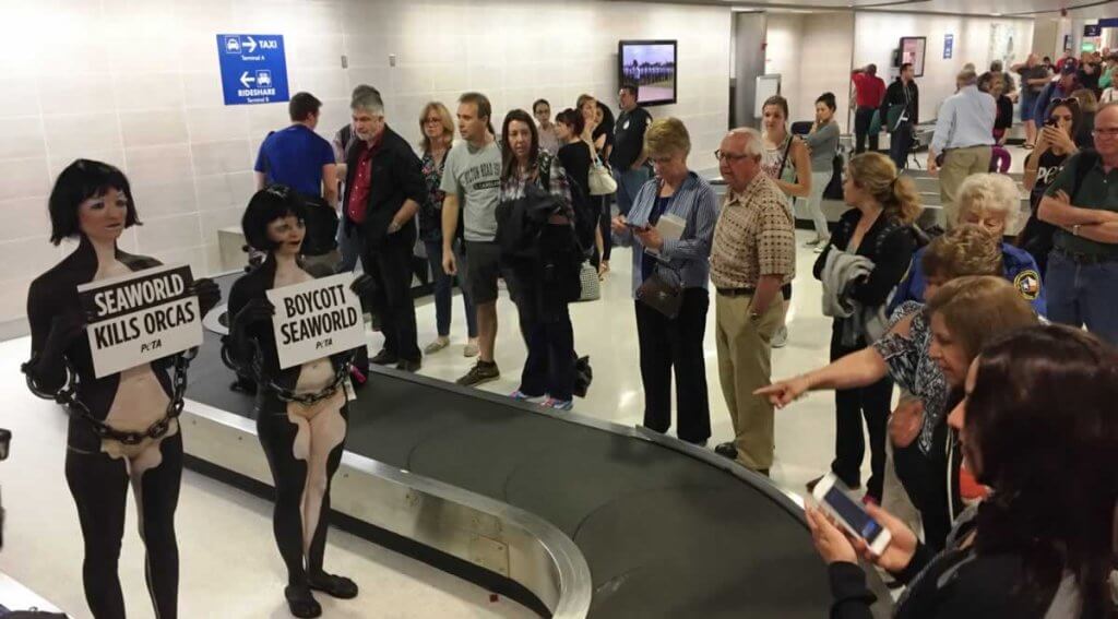 A group of people standing in front of a luggage carousel.