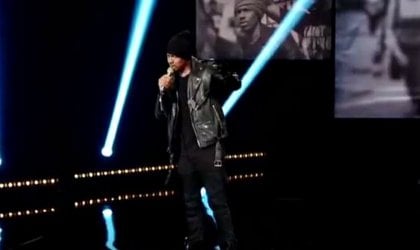 Nick Cannon, wearing a leather jacket, is singing on stage.
