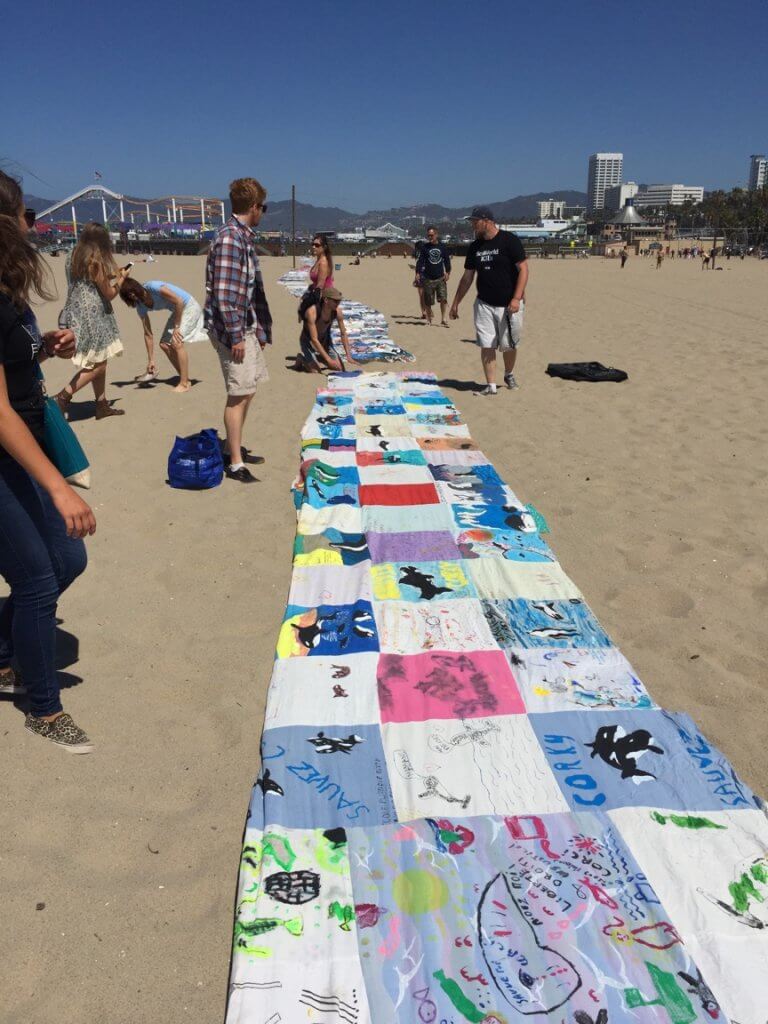 A group of people standing around a large blanket at the beach.