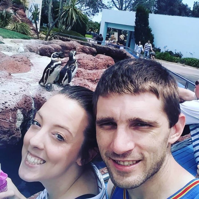 A man and woman taking selfies in front of a penguin exhibit at Seaworld.