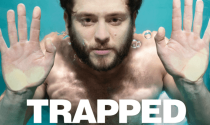 a closeup of Christopher von Uckermann submerged as if in a tank at SeaWorld with his hands pressed against glass, with the word "Trapped"