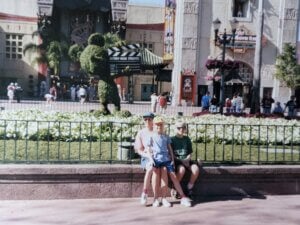 a childhood photo of Melanie Johnson sits on her mother's lap on a bench in front of a bed of flowers at Disney-MGM studios
